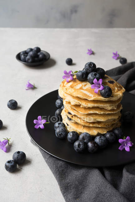 Stapel leckerer Knollen mit Blaubeeren und lila Blüten auf schwarzem Teller auf grauem Hintergrund — Stockfoto