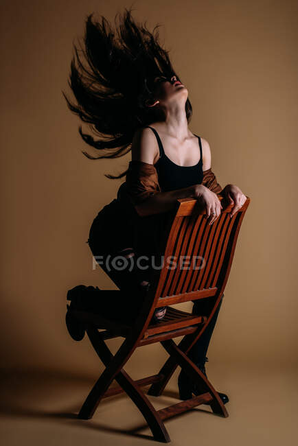 Porträt einer schönen jungen Frau mit langen Haaren, die im Studio sitzt und auf beigen Hintergrund in die Kamera schaut — Stockfoto