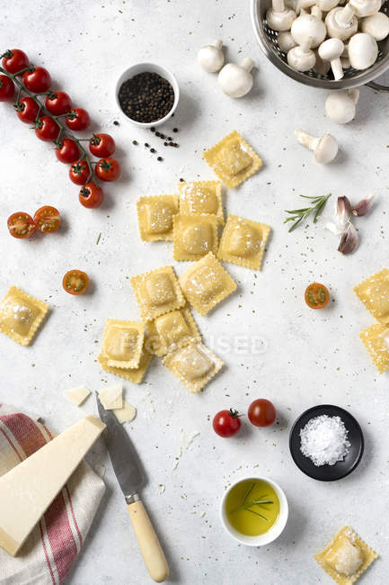 Uncooked ravioli and spices with tomatoes and mushrooms on table — Stock Photo