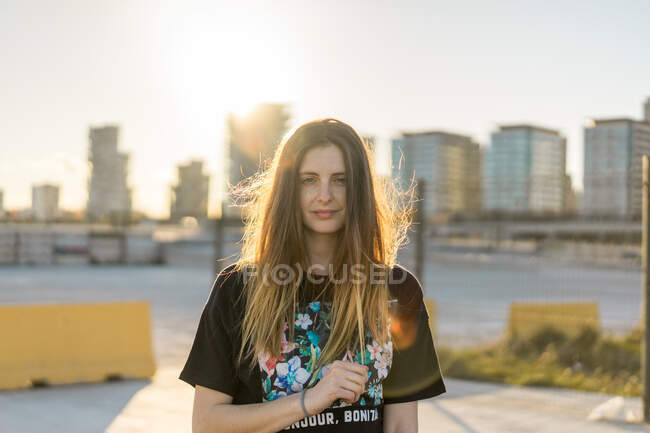 Hübsche junge Frau blickt in die Kamera und steht an sonnigen Tagen vor Wohnhäusern. — Stockfoto