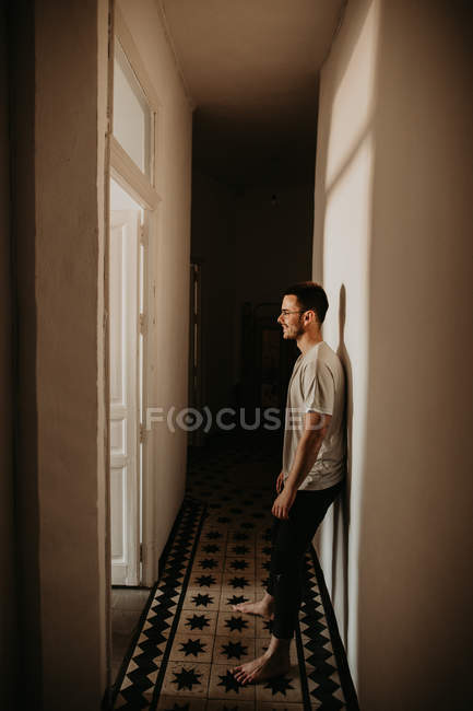 Seitenansicht eines fröhlichen Mannes, der sich an die Wand lehnt und zu Hause im Flur wegsieht — Stockfoto