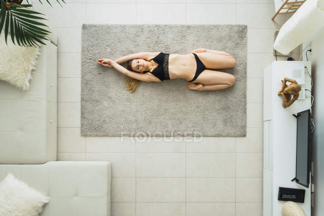 Расслабленная женщина в черном белье в йоге лежит на ковре дома — стоковое фото