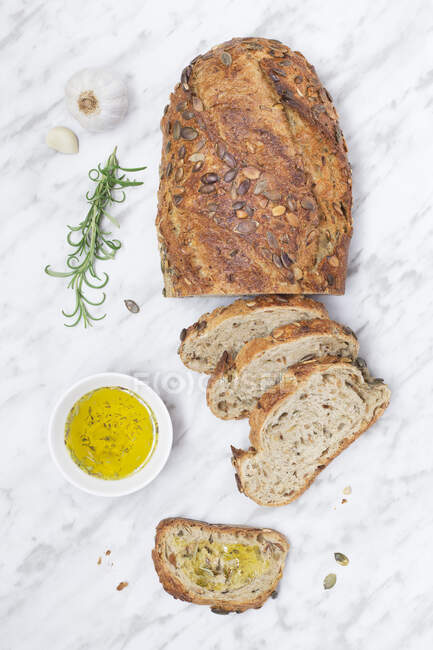 Vista superior de un pan recién horneado con semillas y un tazón de aceite de oliva. - foto de stock