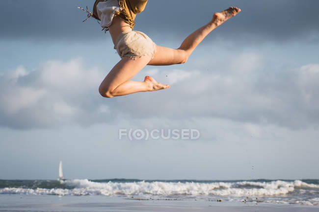 Fille sautant sur la plage avec ciel nuageux sur le fond — Photo de stock