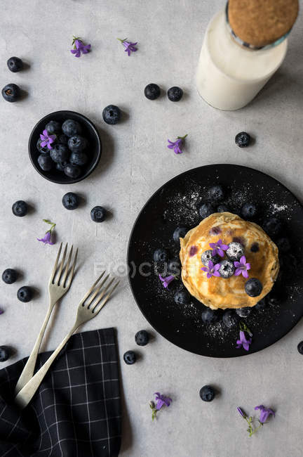Стопка аппетитных вкусных крошек с черникой и фиолетовыми цветами на черном фоне — стоковое фото