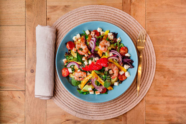 Vegetable salad with shrimps in blue bowl on mat — Stock Photo