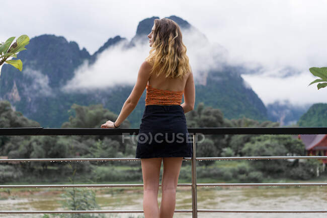 Femme penchée dans les mains courantes regardant les montagnes — Photo de stock