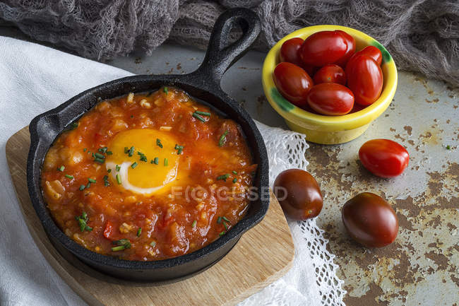 Fried egg with tomatoes in frying pan on wooden chopping board — Stock Photo