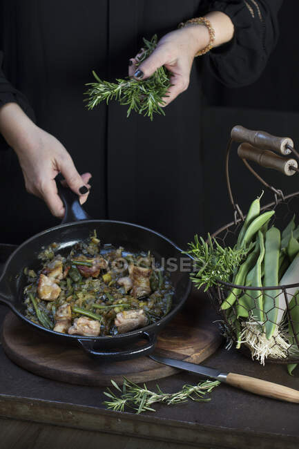 Crop unrecognizable cook putting rosemary to pan with cooking food. — Stock Photo