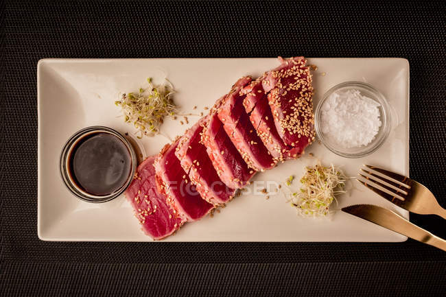 Roh geschnittenes Thunfischsteak auf Platte mit Sauce auf schwarzem Hintergrund — Stockfoto