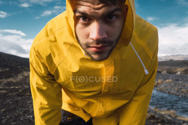 Crop view of young bearded male standing in bright raincoat looking at camera — Stock Photo