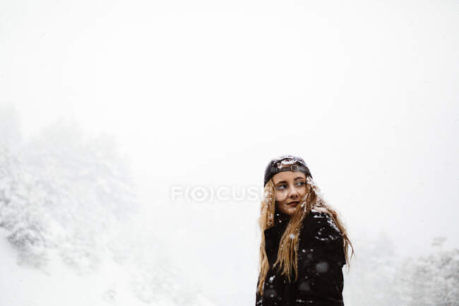 Vista laterale di bella donna in piedi e guardando la fotocamera su strada in nevicata. — Foto stock