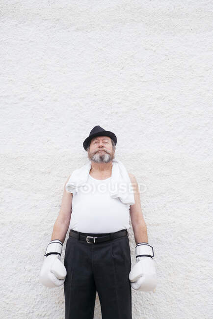 Взрослый мужчина в шляпе и белых боксерских перчатках у грубой стены. — стоковое фото