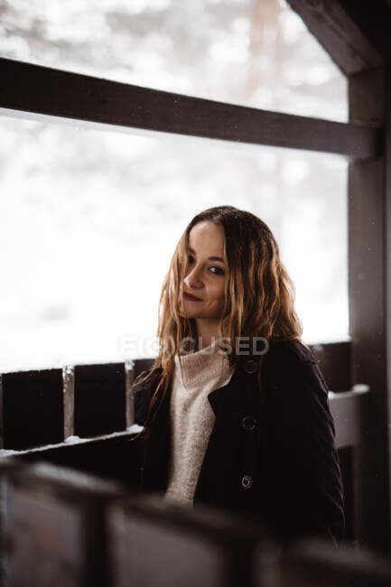Усміхнена красива жінка стоїть на дерев'яному паркані в білий зимовий день . — стокове фото
