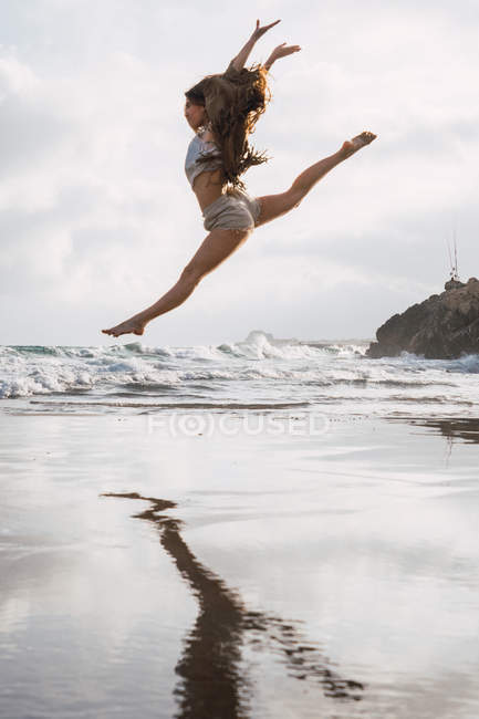 Девушка прыгает на пляже с облачным небом на заднем плане — стоковое фото