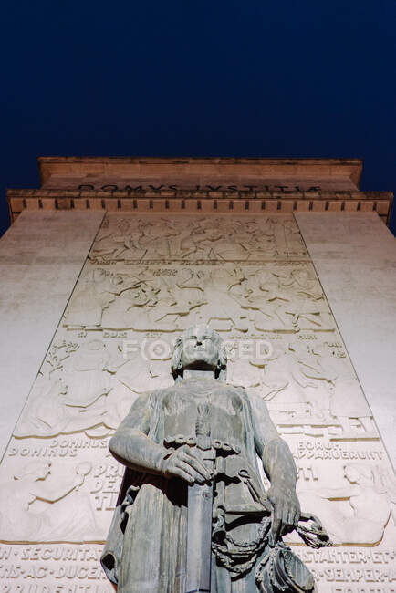 From below big statue holding sword at illuminated wall. — Stock Photo