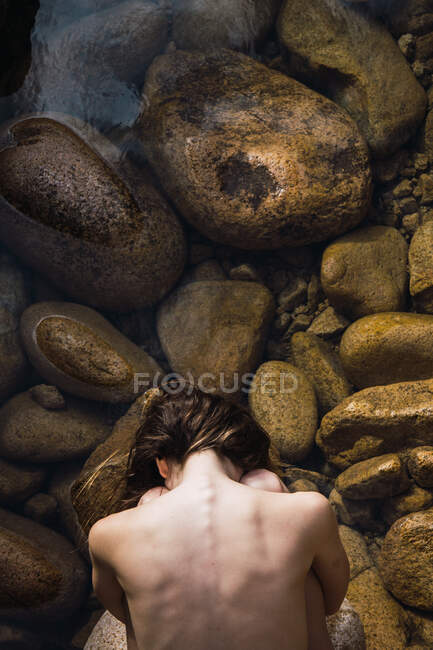 Von oben nackte Frau, die mit den Händen hinter dem Rücken auf Steinen sitzt. — Stockfoto