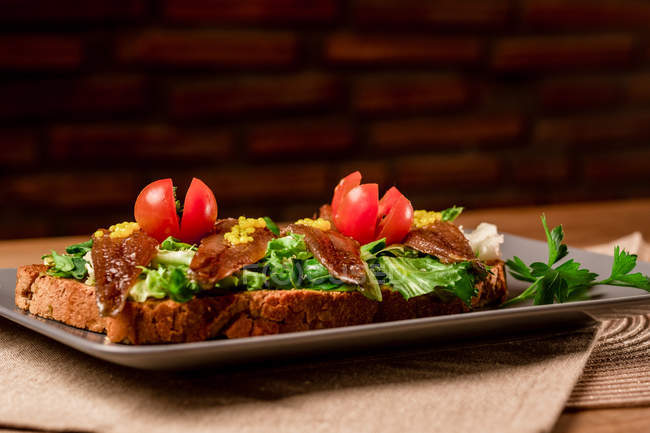 Panino con verdure e pesce su piatto grigio su tavolo di legno — Foto stock