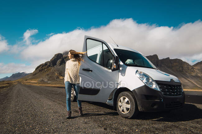 Girl standing on gravel road with white traveling bus on background of mountains in Iceland sunlight. — Stock Photo