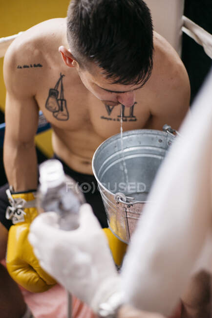 Boxer sportivo sul ring che sputa l'acqua al secchio. — Foto stock