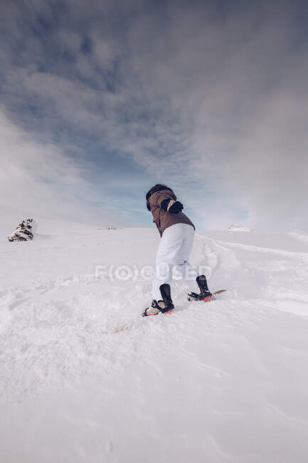 ¿Mujer irreconocible usando ropa de abrigo y snowboard con munición especial deslizándose cuesta abajo? sobre fondo nublado del cielo - foto de stock