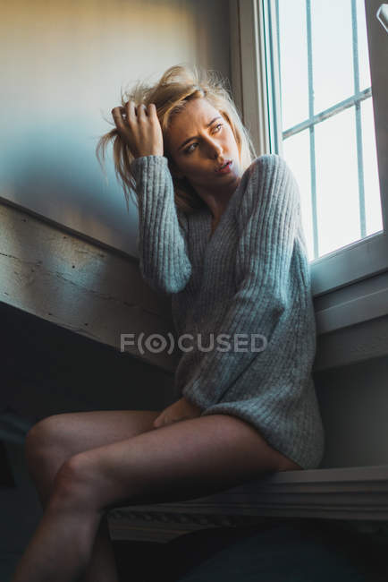 Blonde young thoughtful woman in sweater sitting at window — Stock Photo