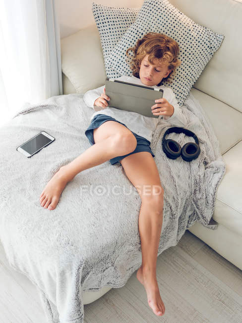 Chico aburrido usando tableta digital en el sofá - foto de stock