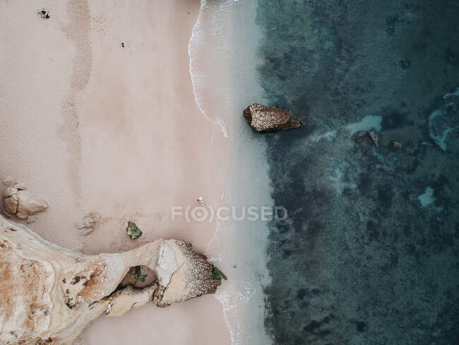 Верхний вид с беспилотника белого песчаного пляжа с камнями и камнями, омытыми кристально чистой волной океана — стоковое фото