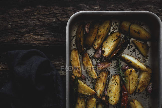 Roasted golden crunchy potato wedges in baking pan on wooden table — Stock Photo