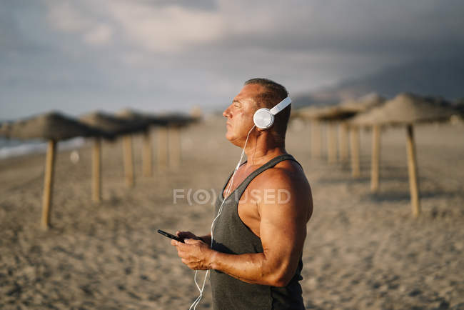 Älterer Mann hört Musik am Strand — Stockfoto