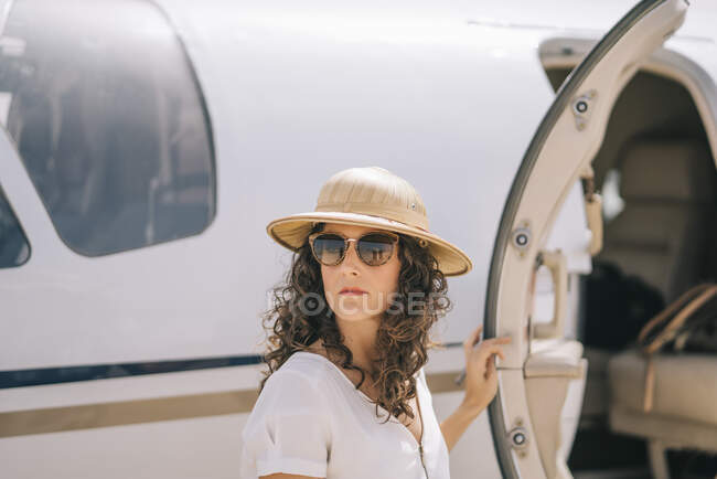 Красуня з сонцезахисними окулярами і капелюхом біля літака.. — стокове фото