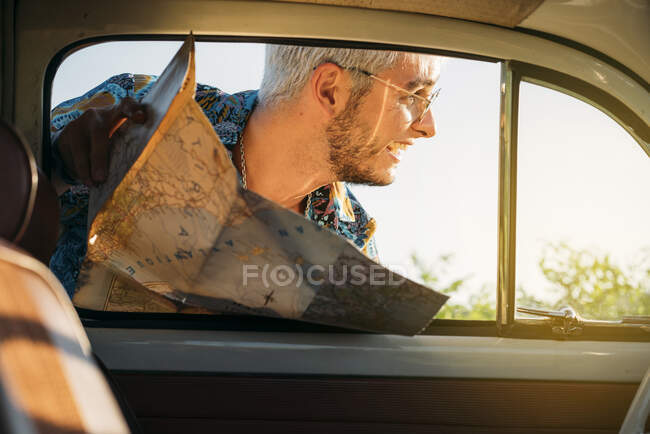 Homem alegre com mapa olhando para fora de um carro — Fotografia de Stock