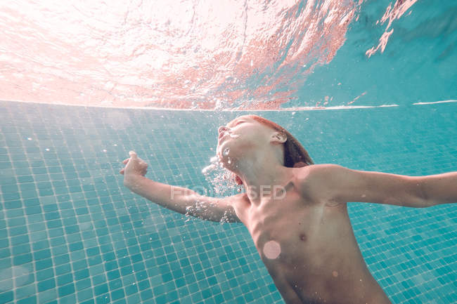 Menino mergulhando na água da piscina azul transparente — Fotografia de Stock