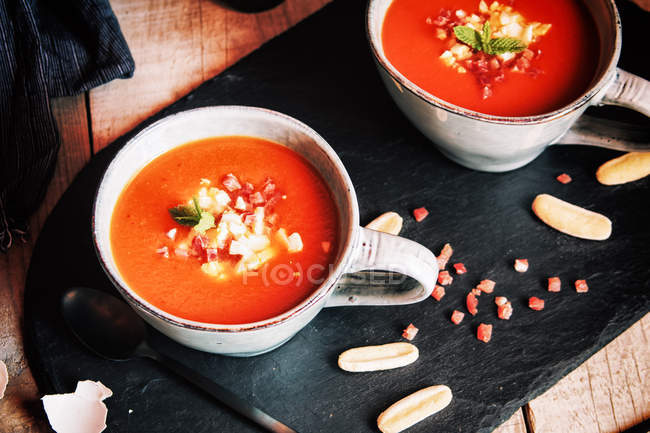 Tomato gazpacho served with egg and ham in cups on slate — Stock Photo