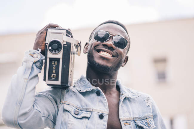 Улыбающийся черный мужчина в солнцезащитных очках держит винтажное радио устройство — стоковое фото