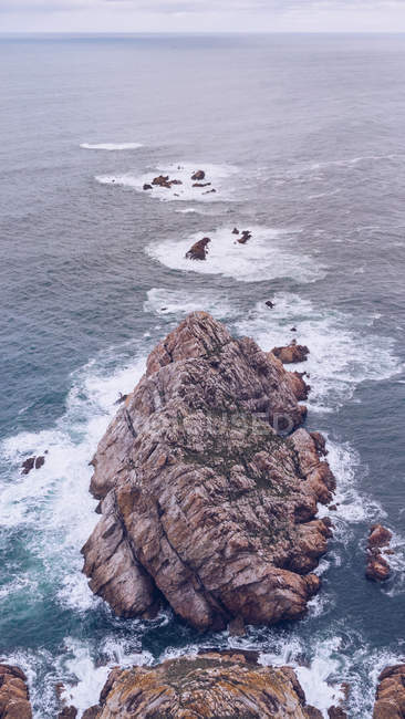Pintoresca vista de drones de agua de mar salpicando alrededor de un pequeño acantilado en Asturias, España - foto de stock