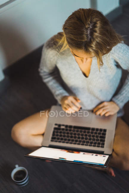 Молодая женщина в свитере печатает на ноутбуке — стоковое фото