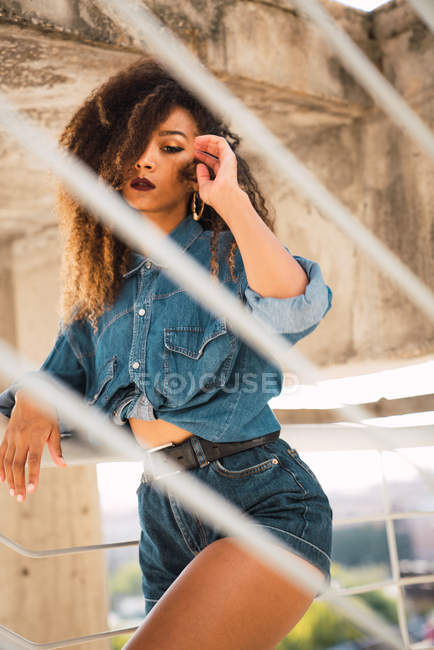 Mujer afroamericana en ropa de mezclilla de pie cerca de la barandilla - foto de stock