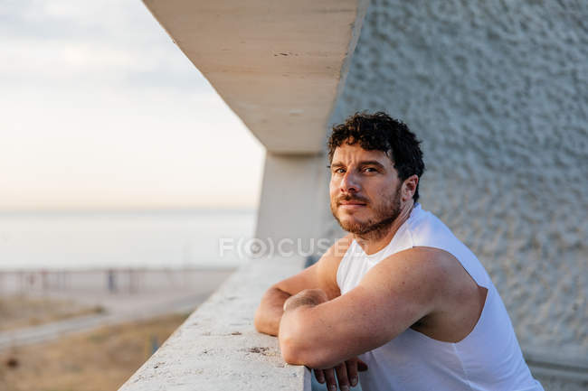 Retrato de homem desportivo pensativo em pé na varanda na praia — Fotografia de Stock