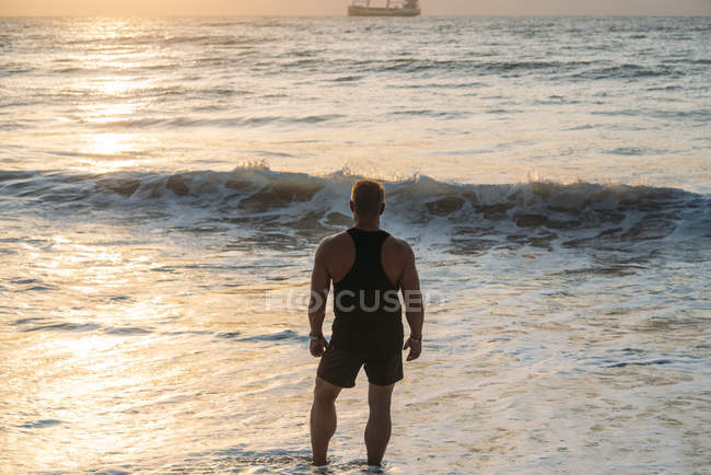 Homem velho forte que se inclina na baía assistindo o pôr do sol na praia — Fotografia de Stock