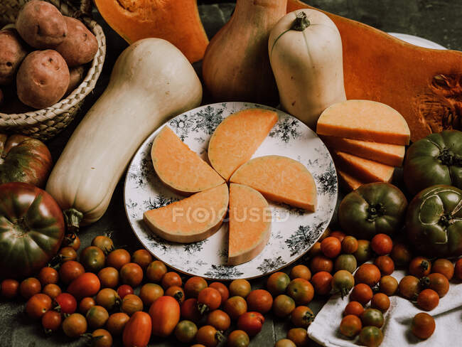 Belo arranjo quente de abóboras maduras na mesa com pequenos tomates e prato com fatias — Fotografia de Stock
