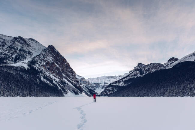 View at distance of anonymous traveler standing in spacious cold snowy field with rocky dark mountains on background — Stock Photo