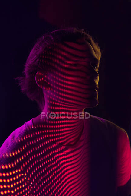 Unrecognizable young guy sitting on stool under red and violet illumination in dark room — Stock Photo