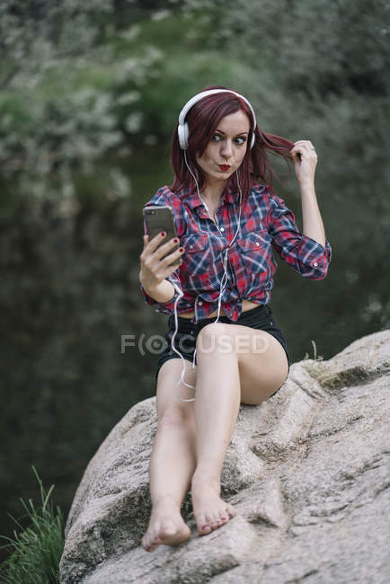 Menina de cabelos vermelhos ouve música junto ao rio — Fotografia de Stock