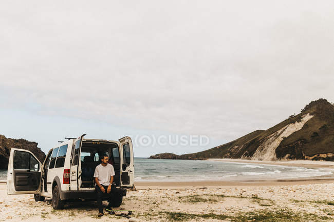 Ragazzo in abito casual guardando lontano mentre seduto vicino furgone bianco sullo sfondo del mare incredibile — Foto stock