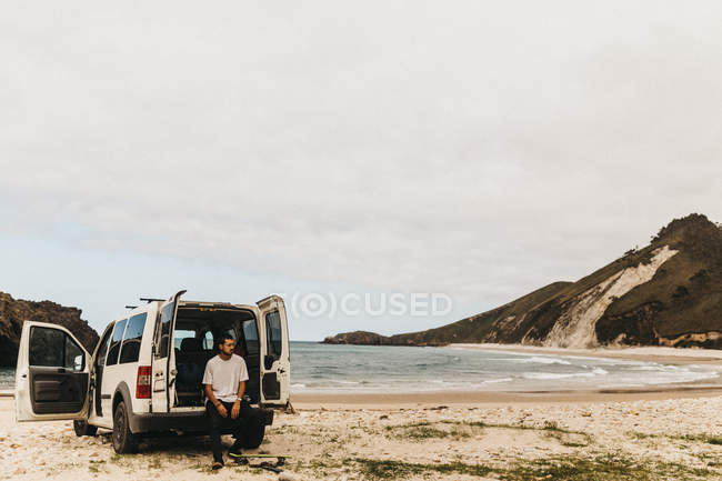 Chico en traje casual mirando hacia otro lado mientras está sentado cerca de la camioneta blanca en el fondo del mar increíble - foto de stock