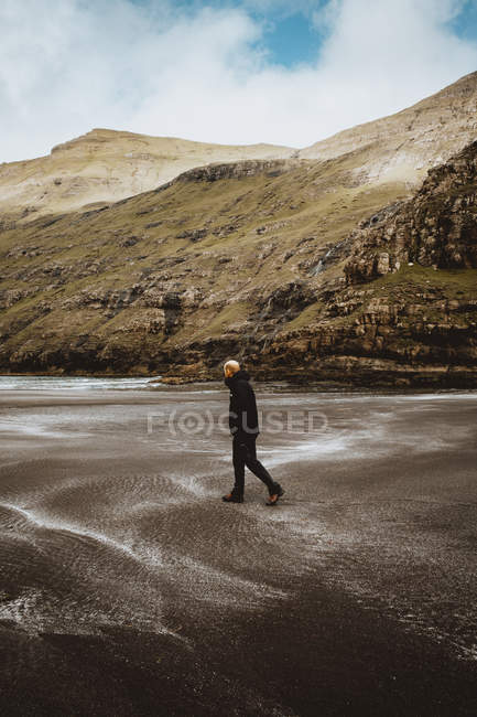 Homme en vêtements chauds debout sur le rivage de l'océan calme avec des falaises sur bacground sur les îles Feroe — Photo de stock