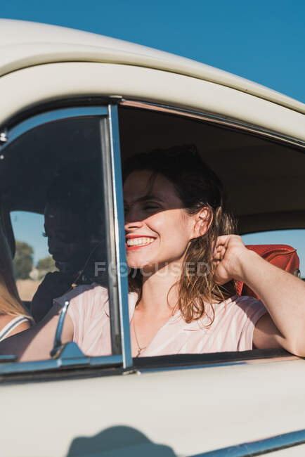 Подружки сидять в ретро-автомобілі і їздять на природі з яскравим сонячним світлом, подорожуючи разом влітку — стокове фото