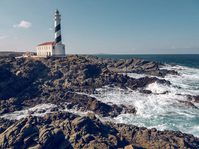 View to tower of lighthouse on rocky coast and blue ocean in sunny day. — Stock Photo