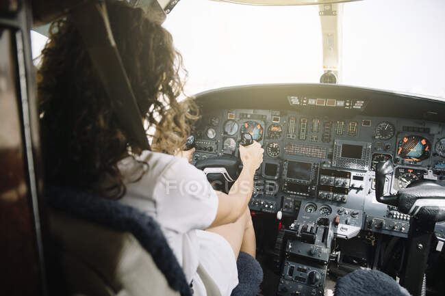 Rückansicht einer brünetten Frau mit lockigem Haar, die im Cockpit sitzt und das Flugzeug steuert — Stockfoto